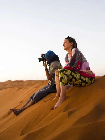 two-people-sitting-top-dune-taking-photos